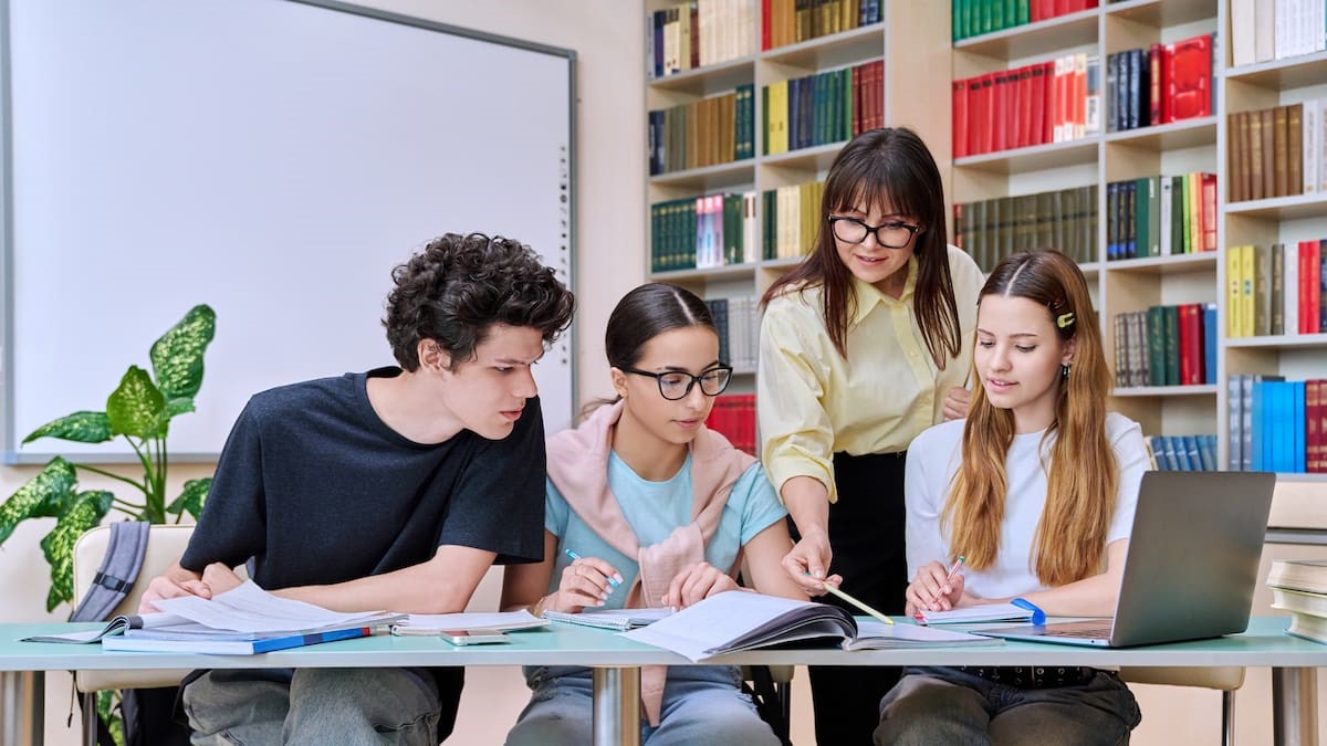Grupo de estudiantes adolescentes con profesora estudian en Biblioteca de aula